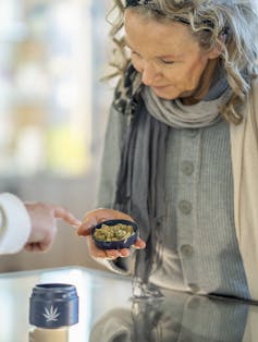 A woman stands at the counter of a legal cannabis retailer as she holds out a lid of buds.