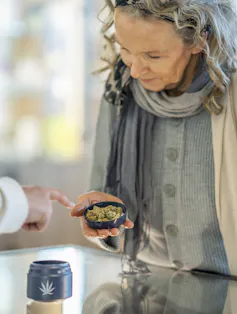 A woman stands at the counter of a legal cannabis retailer as she holds out a lid of buds.