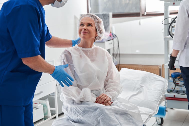 A woman in a surgical cap and gown being prepared for surgery.
