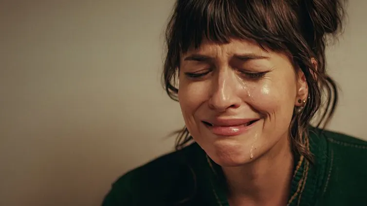 Close up of a sad white woman in her 30s with brown hair, tears streaming down her face and eyes closed.