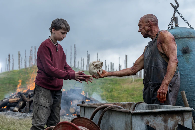 Ralph Fiennes hands Alfie Williams a skull.