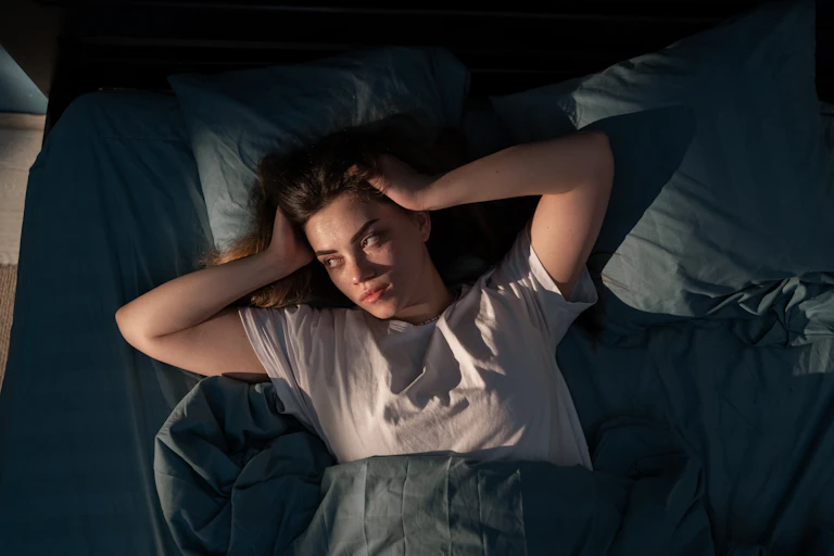 A woman lies awake in bed looking frustrated because she can't sleep.