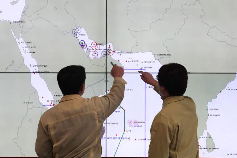 Two men in military uniform examine a map of the Strait of Hormuz.