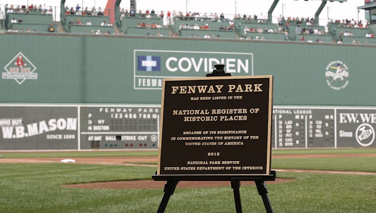 A plaque honoring Fenway Park is displayed on an easel on a baseball field.