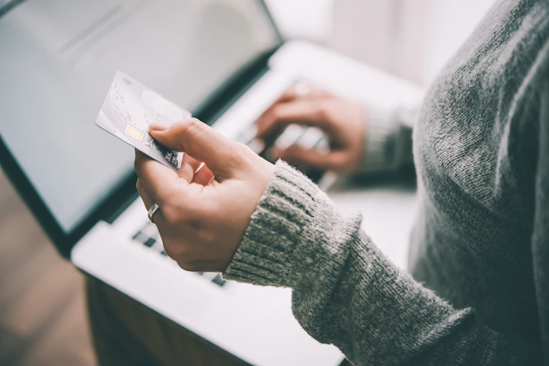 woman's hands holding a credit card and using a laptop to make a purchase.