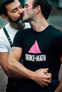 Deux hommes s’embrassent, l’un porte un T-shirt noir avec le slogan silence = death