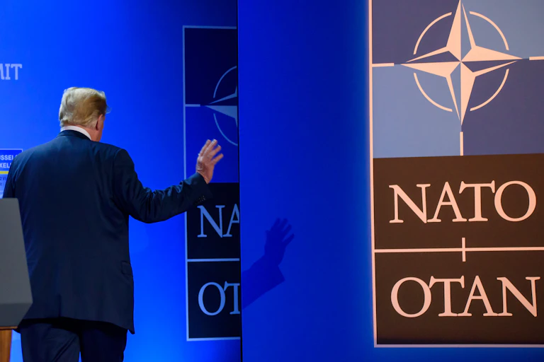 Donald Trump walking away from a lectern and Nato sign