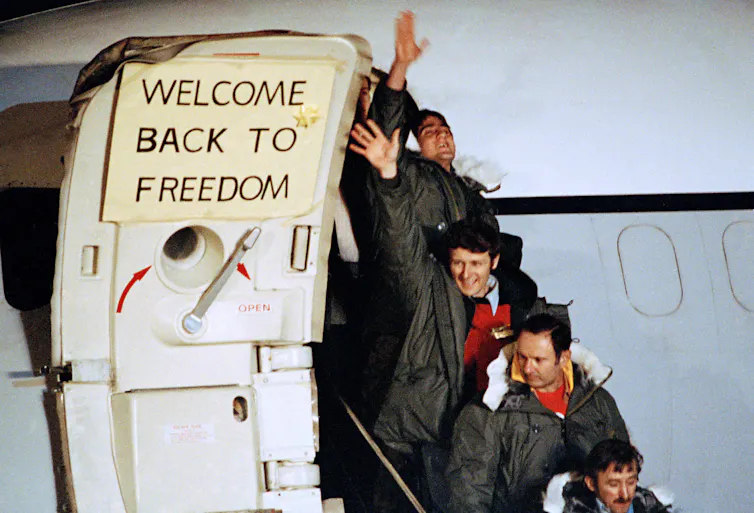 Four men walk down aircraft stairs, with a sign on the airplane door that reads: 'welcome back to freedom.'
