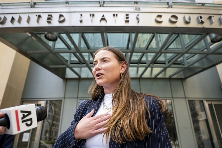 A blonde woman in a blazer speaks to reporters outside a courthouse