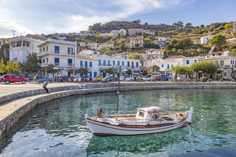 A small boat floats in blue-green waters in front of a picturesque village.