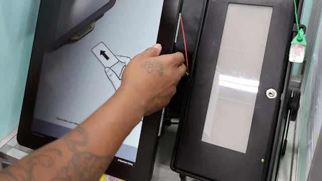an arm extends, hand on the edge of the larger of two side-by-side vertical display screens