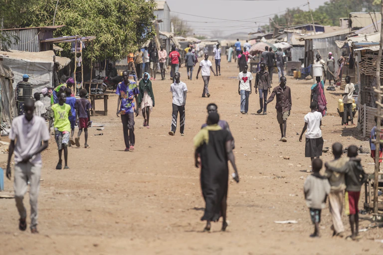 People walk down a wide and dusty street.