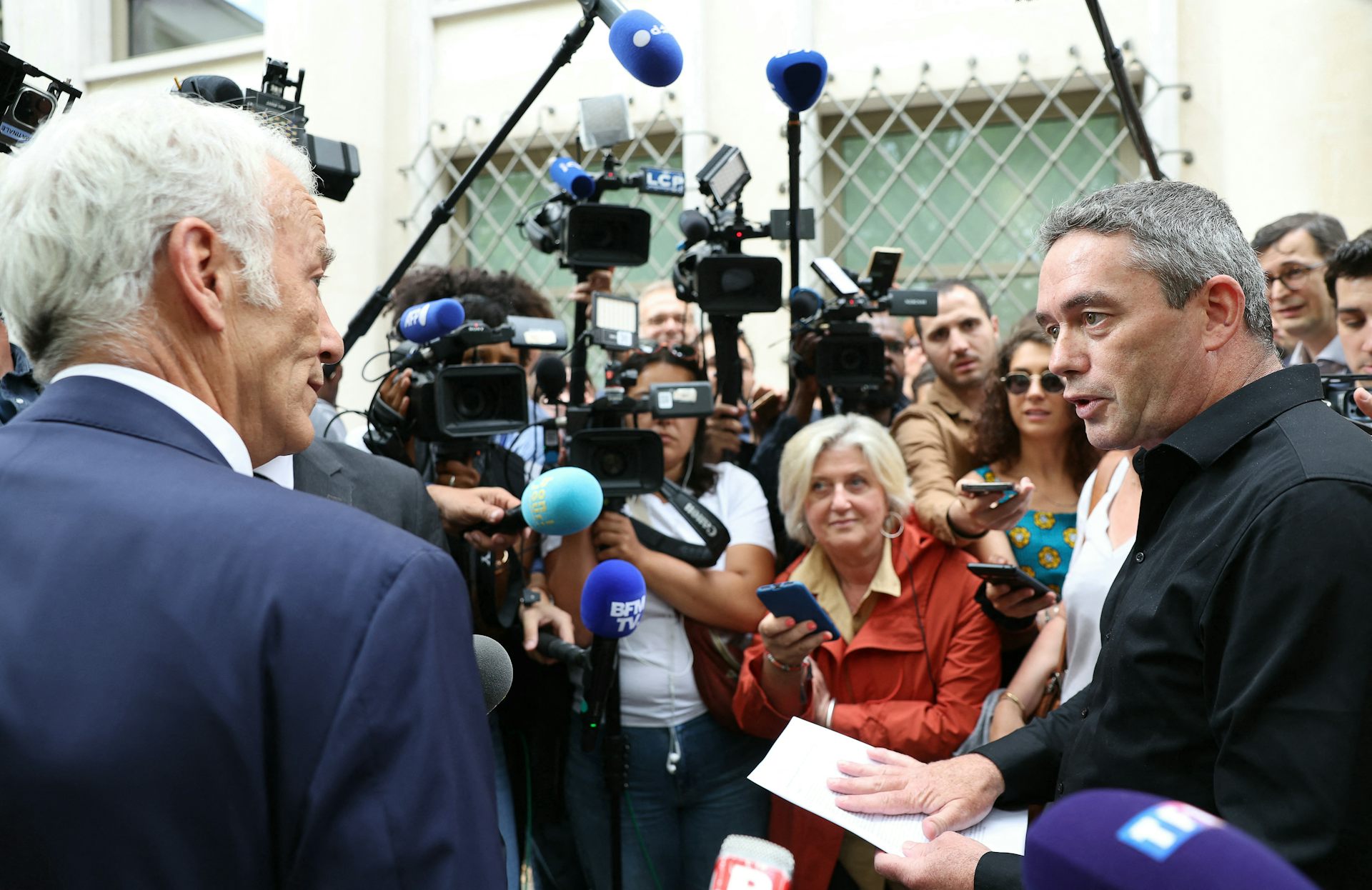 Deux hommes se font face devant les caméras et micros de télévision. 