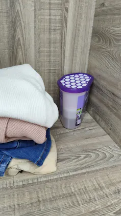A shelf in a wardrobe with a purple box with white powder inside in the corner.