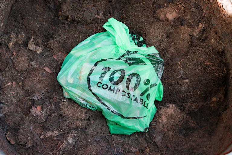 Sac en plastique indiquant « 100 % biodégradable » dans du compost.