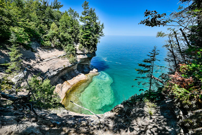 A beach on the side of a lake, featuring blue water and green trees.