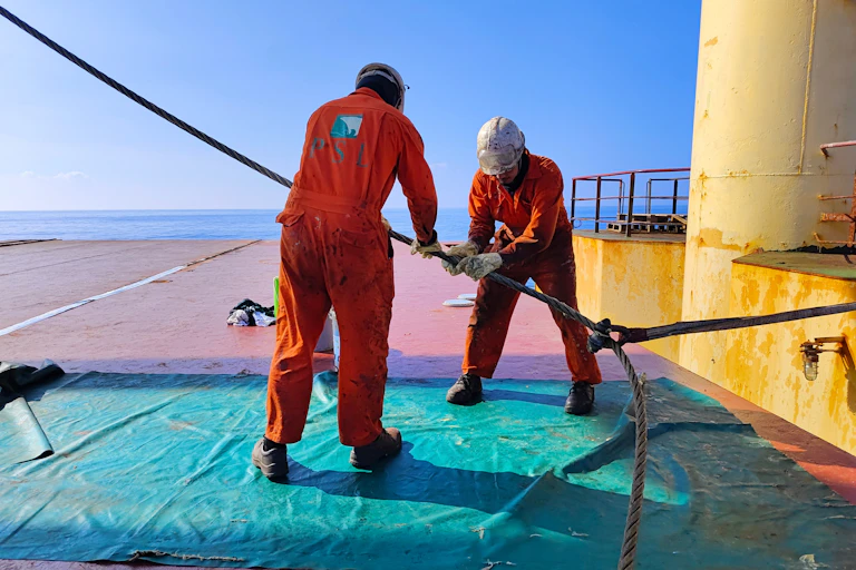 Dos personas en la cubierta de un barco manejando una cuerda