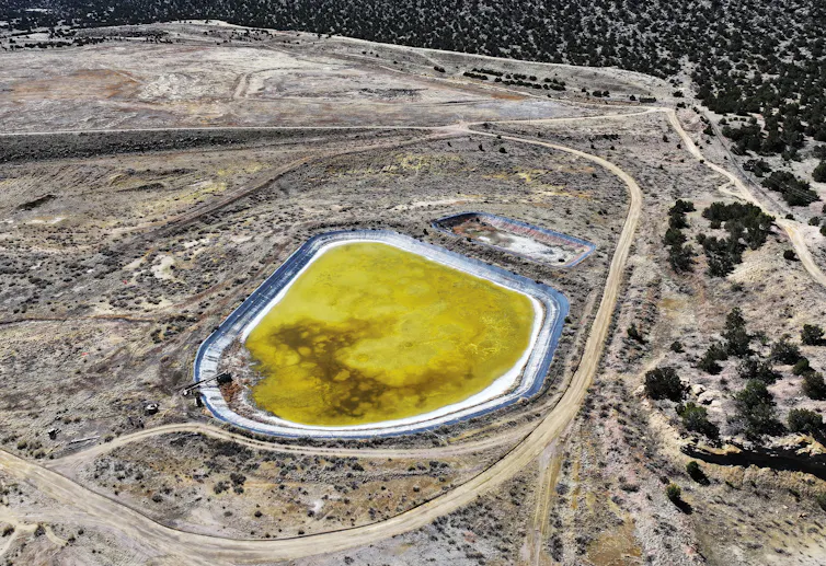 A stretch of barren land, marked by dirt roads around a bright yellow pond.