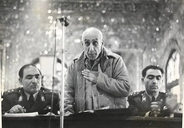 Iran’s historical past has been blighted by means of interference from overseas powers 2 An elderly man holds his hand over his heart, flanked by men in military uniform.