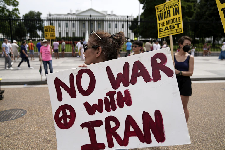 Mulher carregando uma faixa escrito "No War with Iran" em frente à Casa Branca