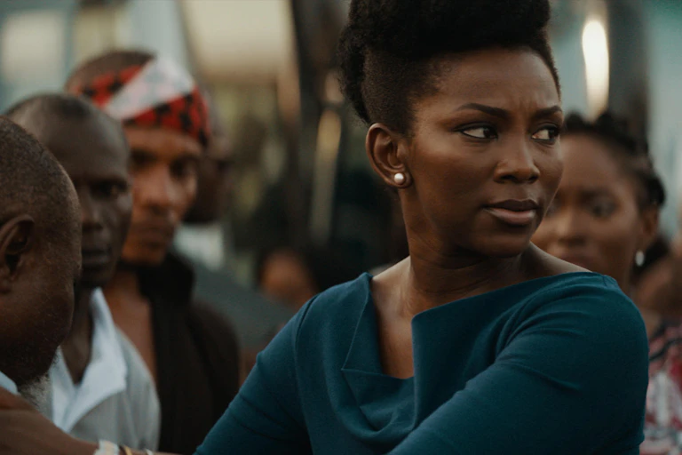 A woman looks angrily at something off camera, arms folded, a group behind her looking at her.