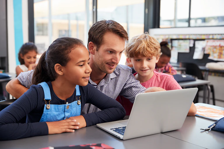 A teacher and two children at a desk using a laptop