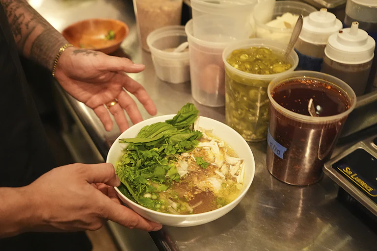 A pair of hands shown holding a bowl of noodle soup over a stainless steel counter