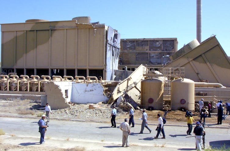 A group of people mill about outside a damaged building.