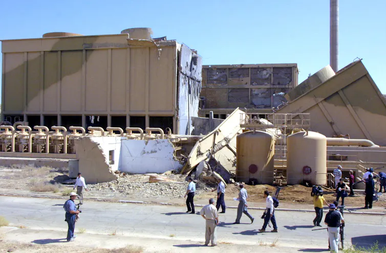 A group of people mill about outside a damaged building.