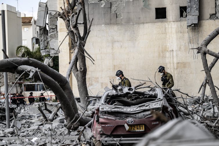 Ceasefires like the only between Iran and Israel ceaselessly fail – however an settlement with particular stipulations is much more likely to carry 1 Two men in uniforms and helmets walking amid the rubble of a bombed building.