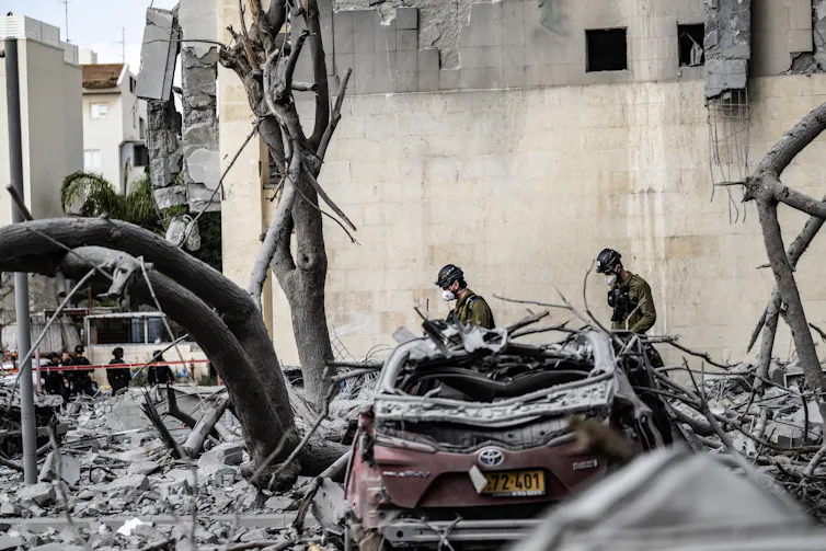 Two men in uniforms and helmets walking amid the rubble of a bombed building.