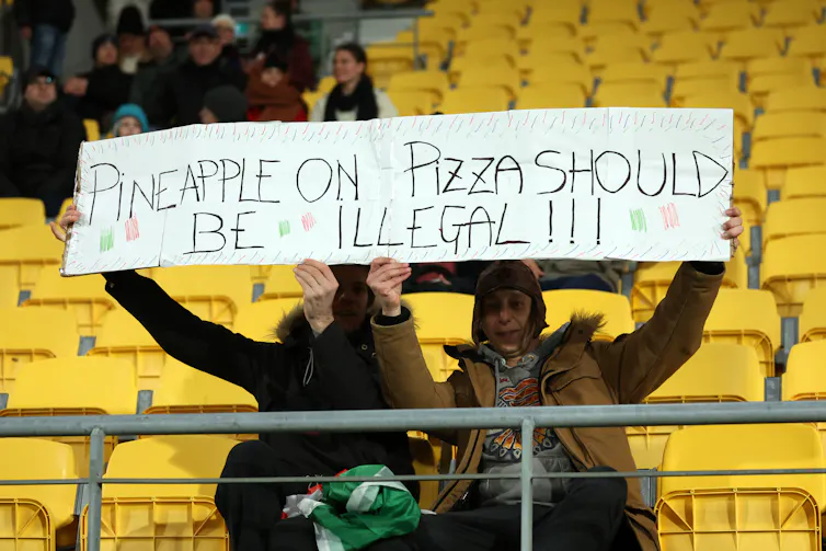 Fans in the stadium at a a soccer game hold a banner reading 'Pineapple on pizza should be illegal!' prior to the FIFA Women's World Cup Australia & New Zealand