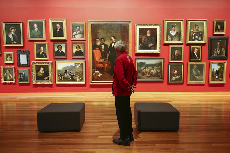 Person stands in front of paintings on a red wall at Te Papa, Wellington.