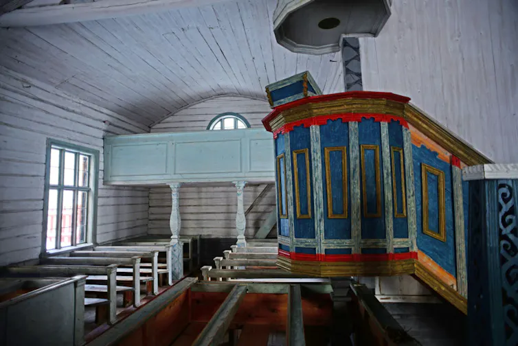 The sanctuary of an old church, painted in white and light blue, with a more brightly colored pulpit.