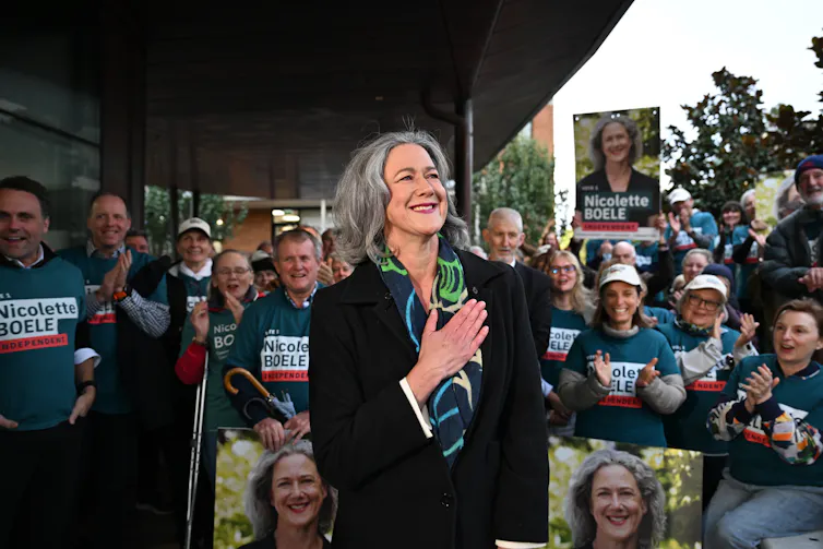 A woman smiles in front of a large crowd holding campaign posters