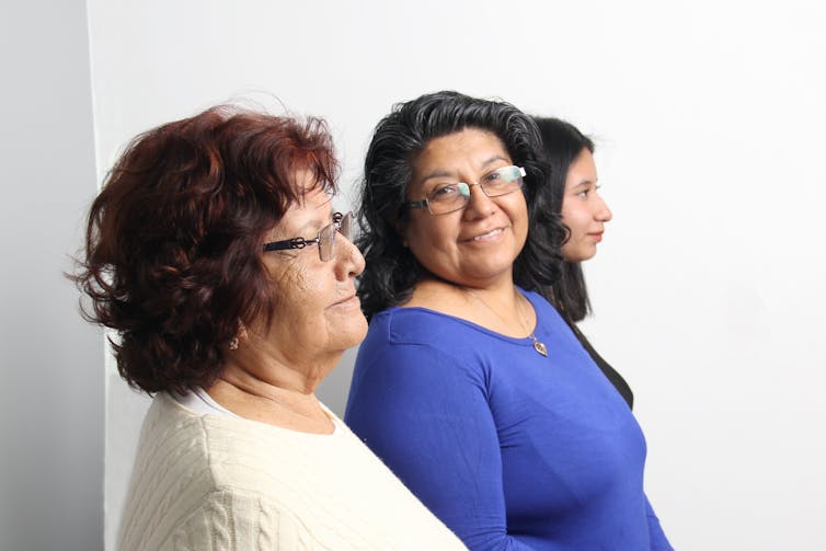 A middle-aged woman in a blue shirt standing between an older woman and teen