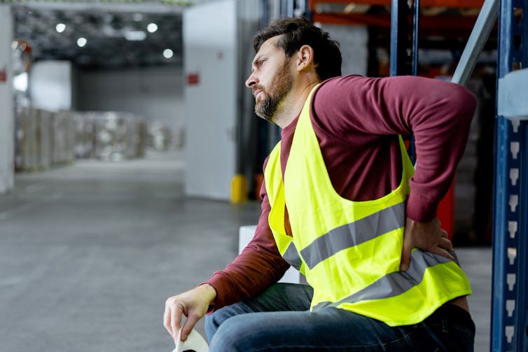 Man holds his back, while sitting at work