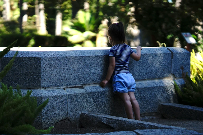 A child looks out over a stone wall outdoors.