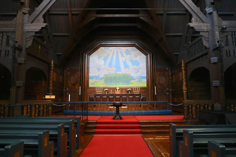 An altar of a church whose walls are made of dark wood, with red carpet running down the center of the room.