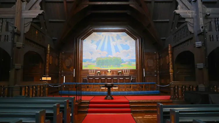 An altar of a church whose walls are made of dark wood, with red carpet running down the center of the room.