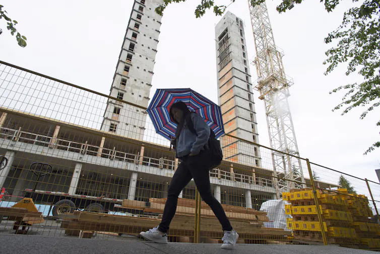 A person with umbrella passes a construction site.