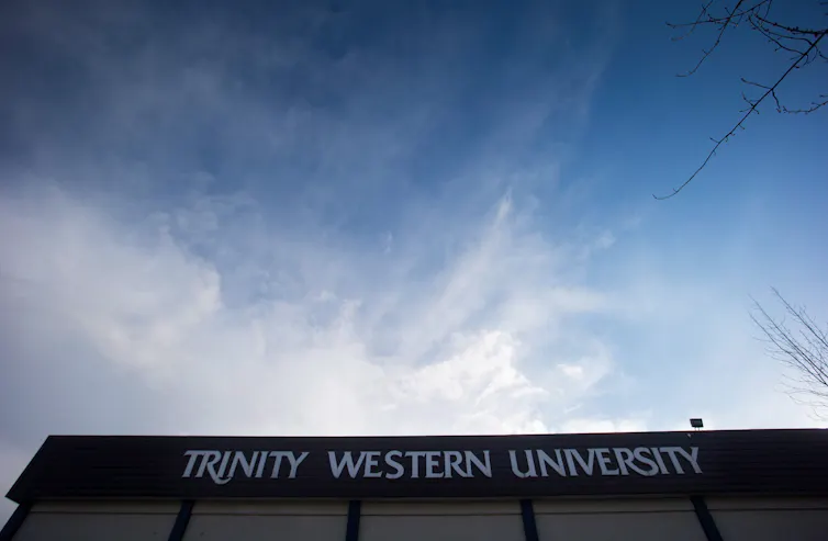 The silhouetted edge of a university building seen beneath a sky with wispy clouds rolling in.