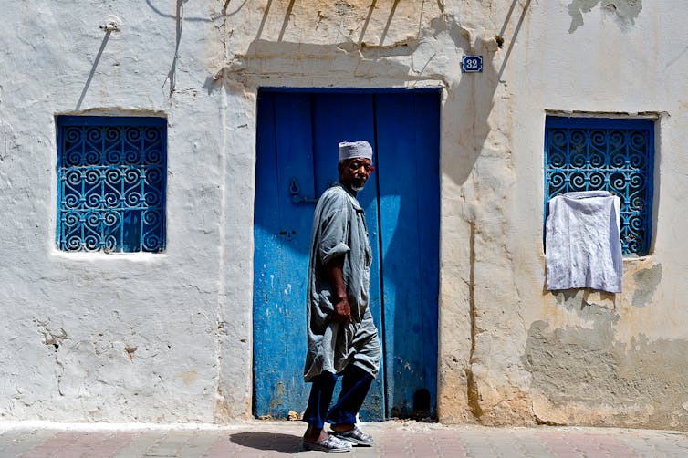 A man wearing traditional dress walks down a street in Djerba.