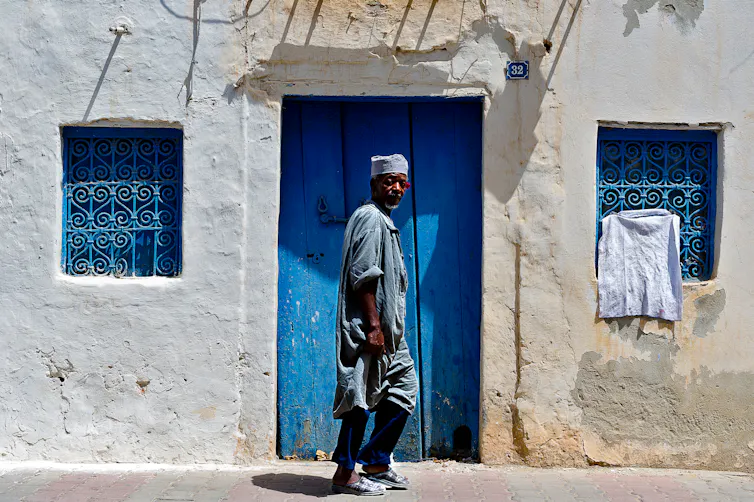 A man wearing traditional dress walks down a street in Djerba.