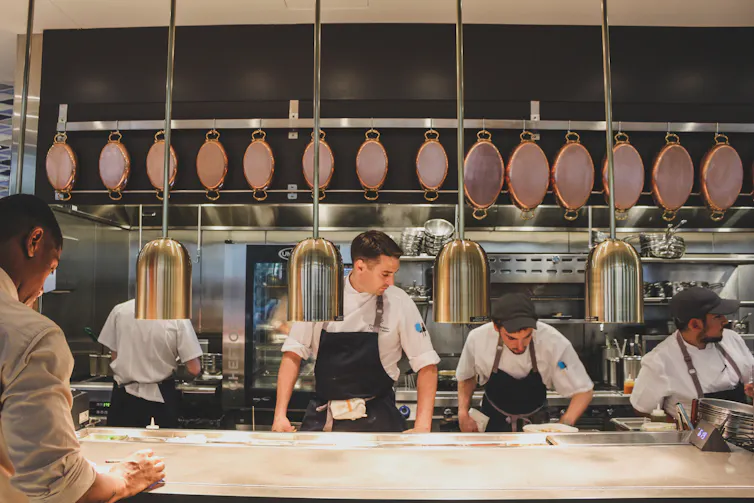 A line of chefs wearing black aprons at work in an open kitchen.