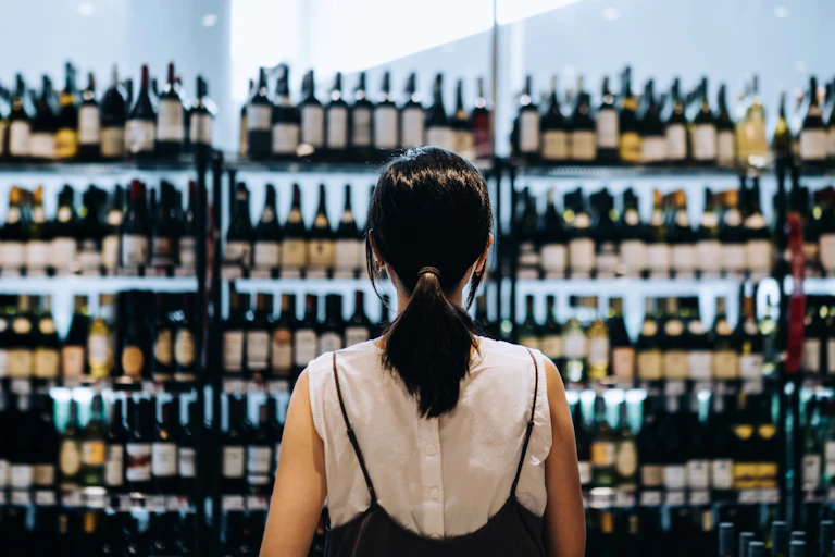 Woman seen from the back looks at a wall of wine bottles.
