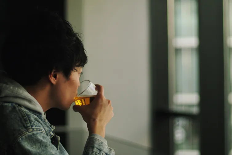 Man looks out the window drinking a beer.