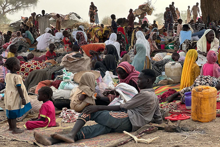 A group of men, women and children lying on the ground surrounded by bags and jerry cans.
