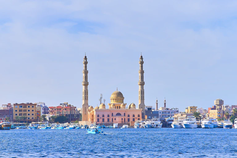 A blue sea in front of ancient brown buildings with minarets and domes