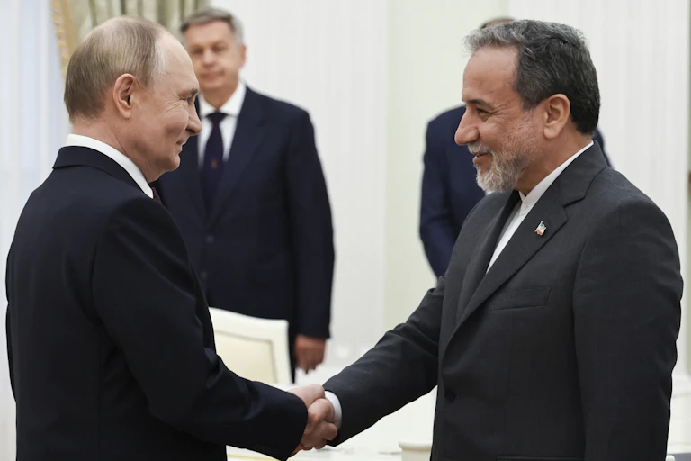 A balding man shakes hand with a dark-haired bearded man. both smile and wear suits.